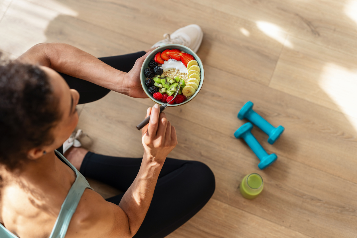 Shot of athletic woman eating a healthy fruit bowl while sitting on floor in the kitchen at home
